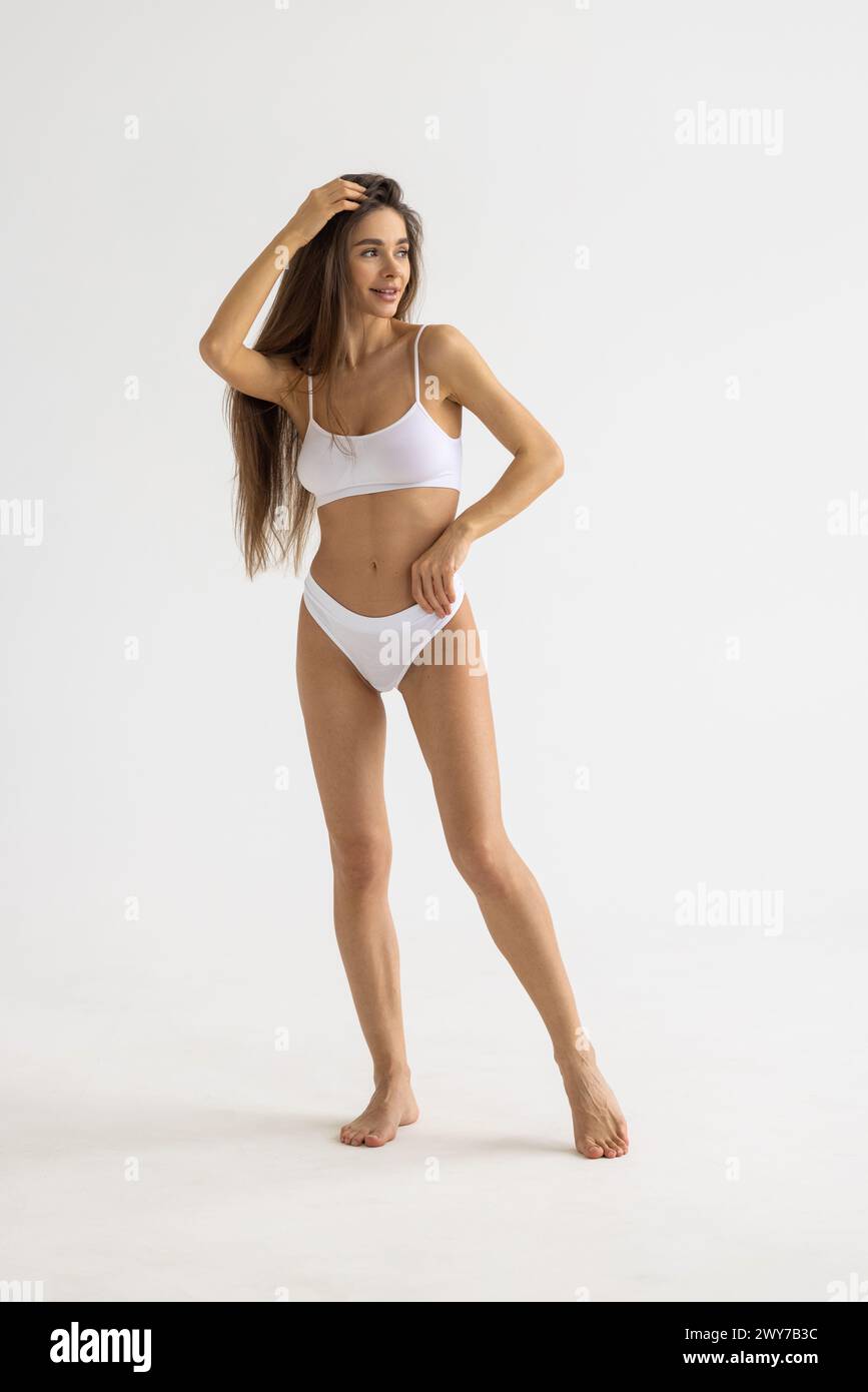 Full lenght portrait of beautiful young fit, slim woman in white underwear, lingerie posing against studio background. Concept of natural beauty, heal Stock Photo