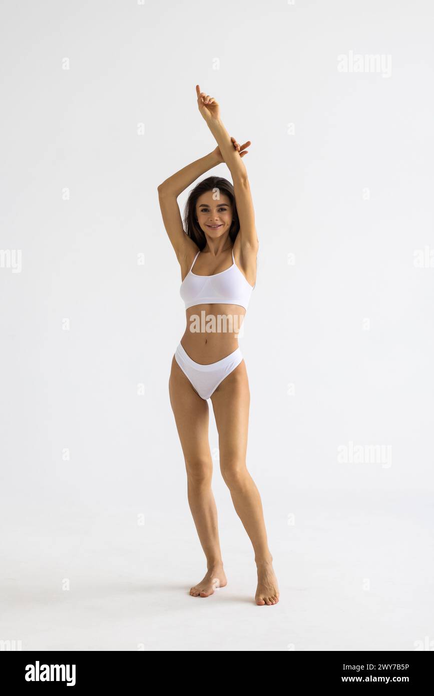 Full lenght portrait of beautiful young fit, slim woman in white underwear, lingerie posing against studio background. Concept of natural beauty, heal Stock Photo