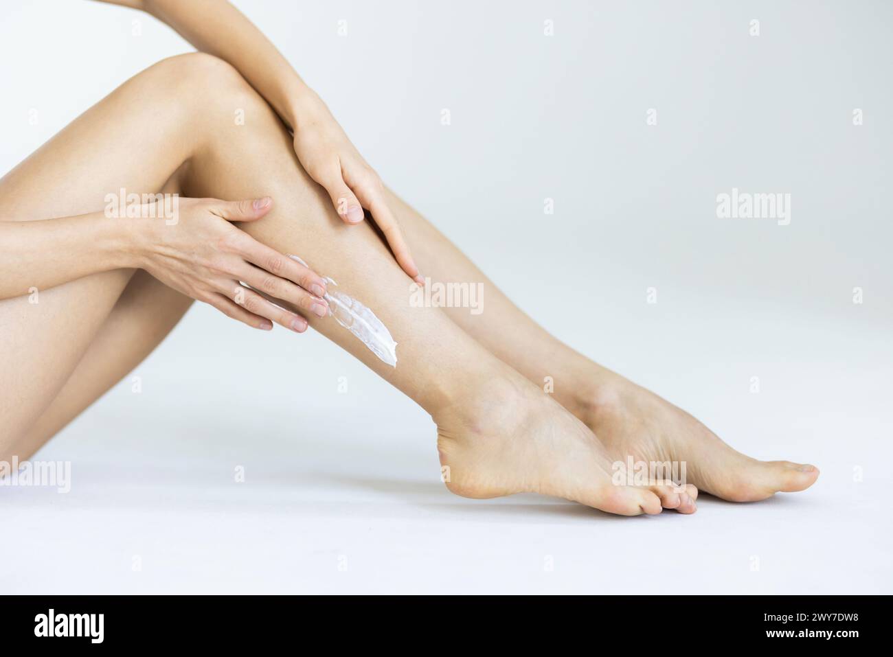 Woman applying body cream onto her smooth legs on light grey background, closeup Stock Photo