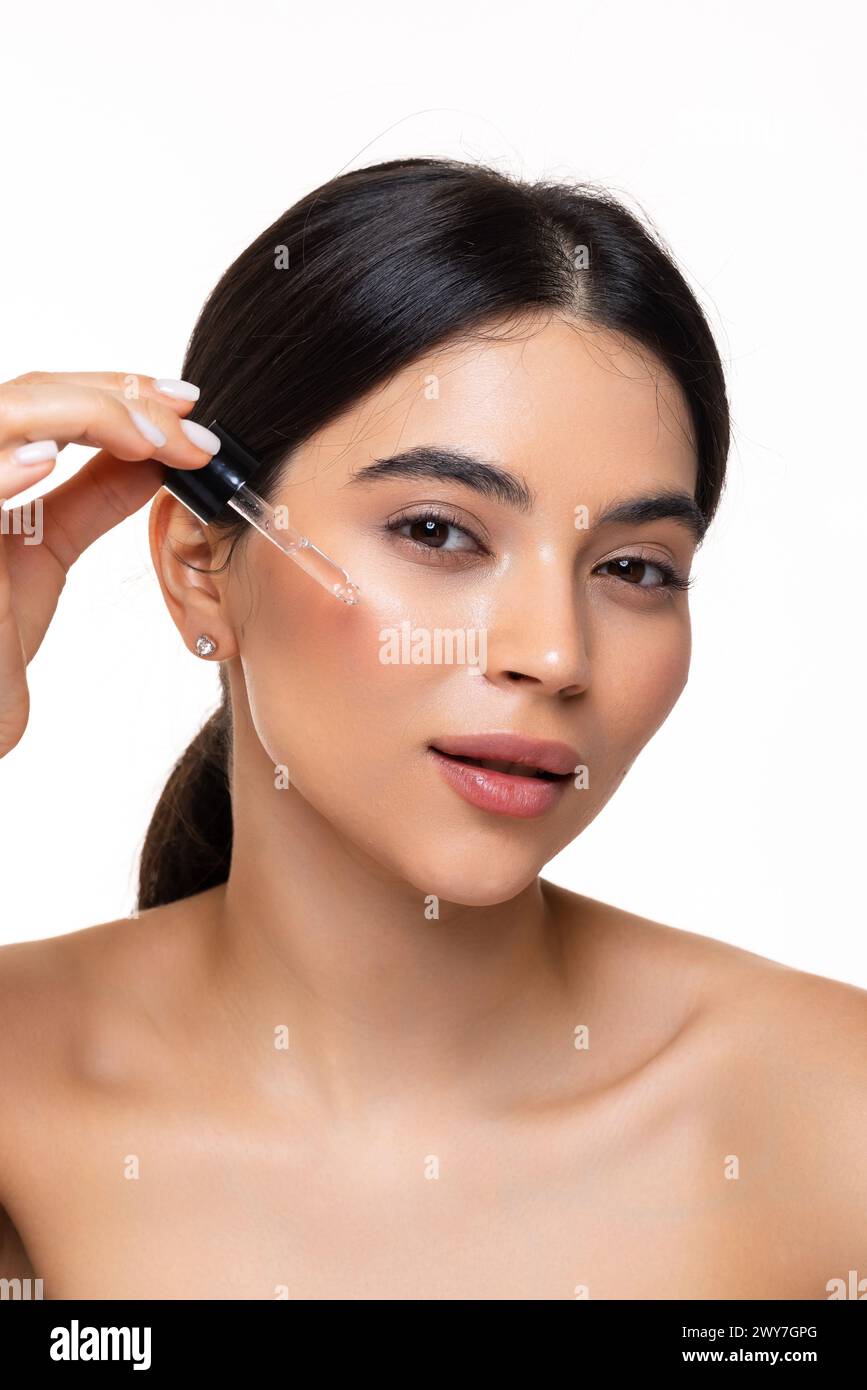 Beauty woman with freckles, naked shoulders and nude face, apply serum vitamin c, argan oil tea tree ingredients in pippette dropper under eye, treati Stock Photo