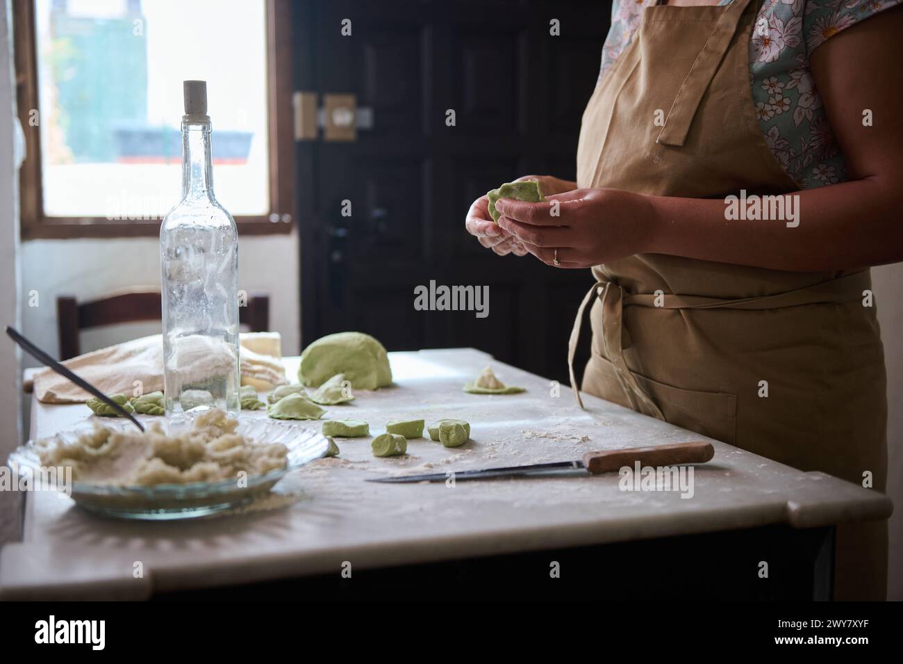 Close-up chef modeling dumplings from spinach dough on the floured surface of a marble table. Preparing varenyky, ravioli. Traditional cuisine and cul Stock Photo
