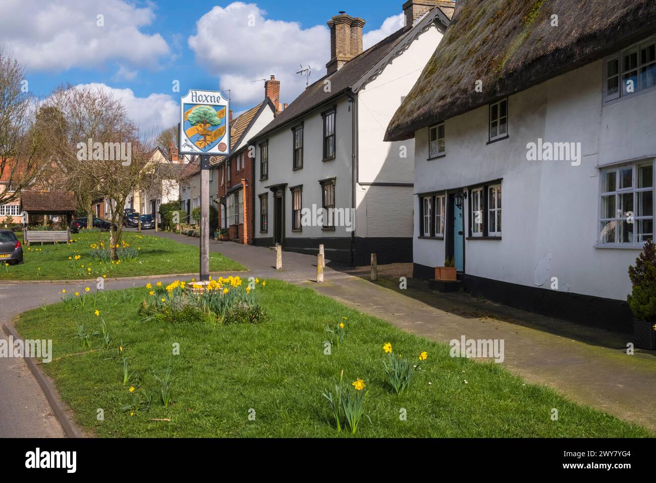 Low Street, Hoxne, Suffolk, East Anglia,UK. The village sign on the green with spring daffodils. Stock Photo