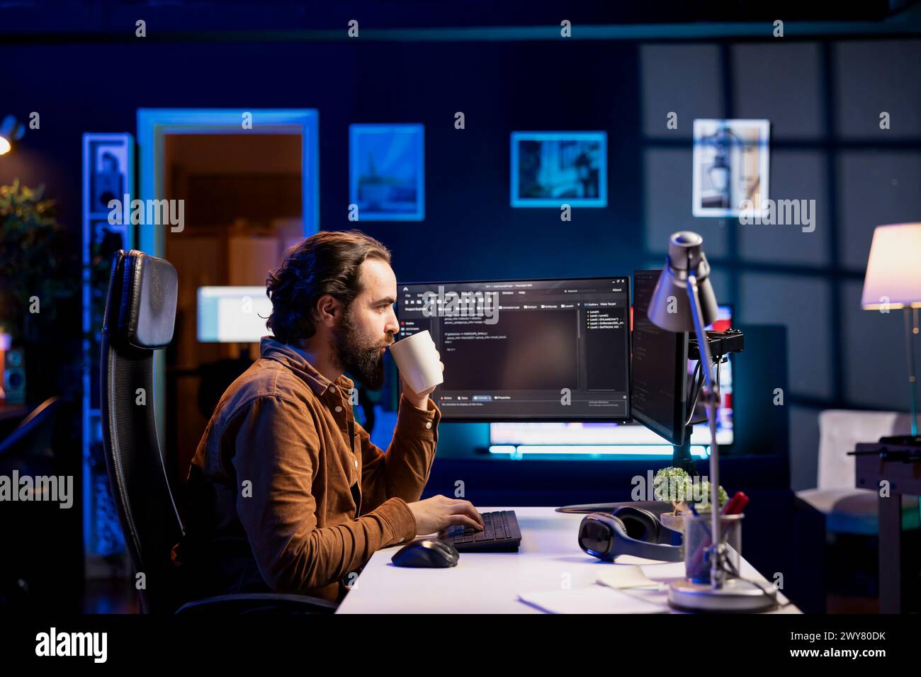 Man drinking coffee while doing software quality assurance, reading source code on computer. Developer inspecting coding on desktop PC and enjoying hot beverage, looking to fix potential issues Stock Photo