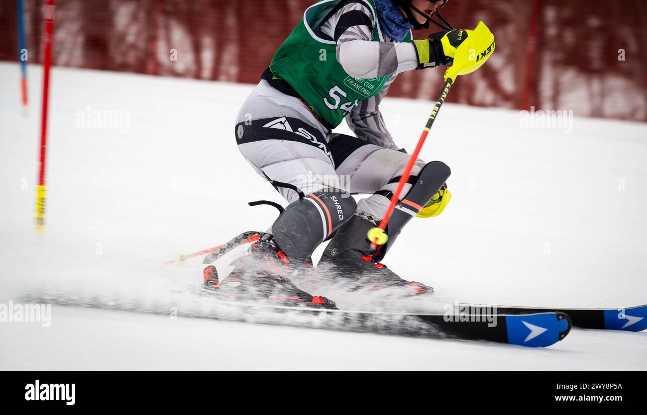 Female U16 Slalom ski racer carving a turn through gate at the end of the racecourse during a March 2024 event, Mittersill race and training slope at Cannon Mountain ski area in the White Mountains, New Hampshire, USA. Stock Photo
