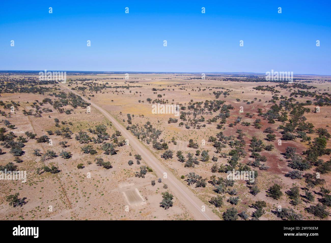 Aerial view of a straight dirt road cutting through a sparsely vegetated desert landscape Stock Photo