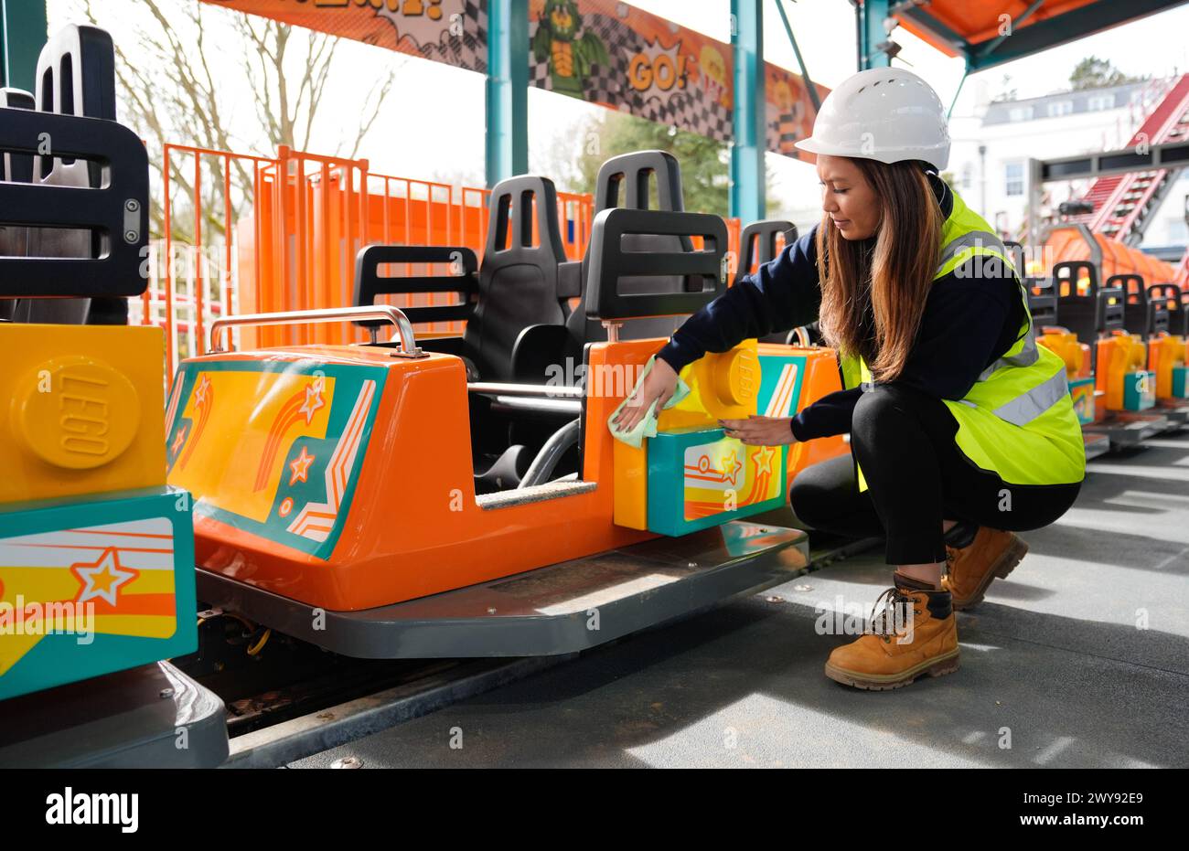 Legoland team member Jenella Tudtud cleans one of the cars on the Minifigure Speedway, as final checks are made to the new ride at Legoland Windsor Resort, in Berkshire. The world's first LEGO duelling coaster, Minifigure Speedway will see riders reach speeds of up to 56km/h as they make their way around the dynamic dual-track. Picture date: Thursday April 4, 2024. Stock Photo