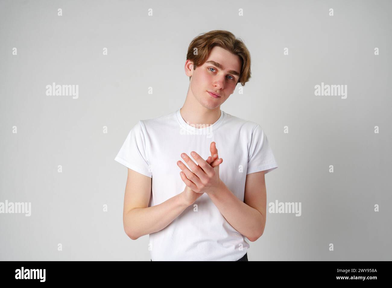 Young Man Clapping Hands in a White T-Shirt Against a Plain Background Stock Photo