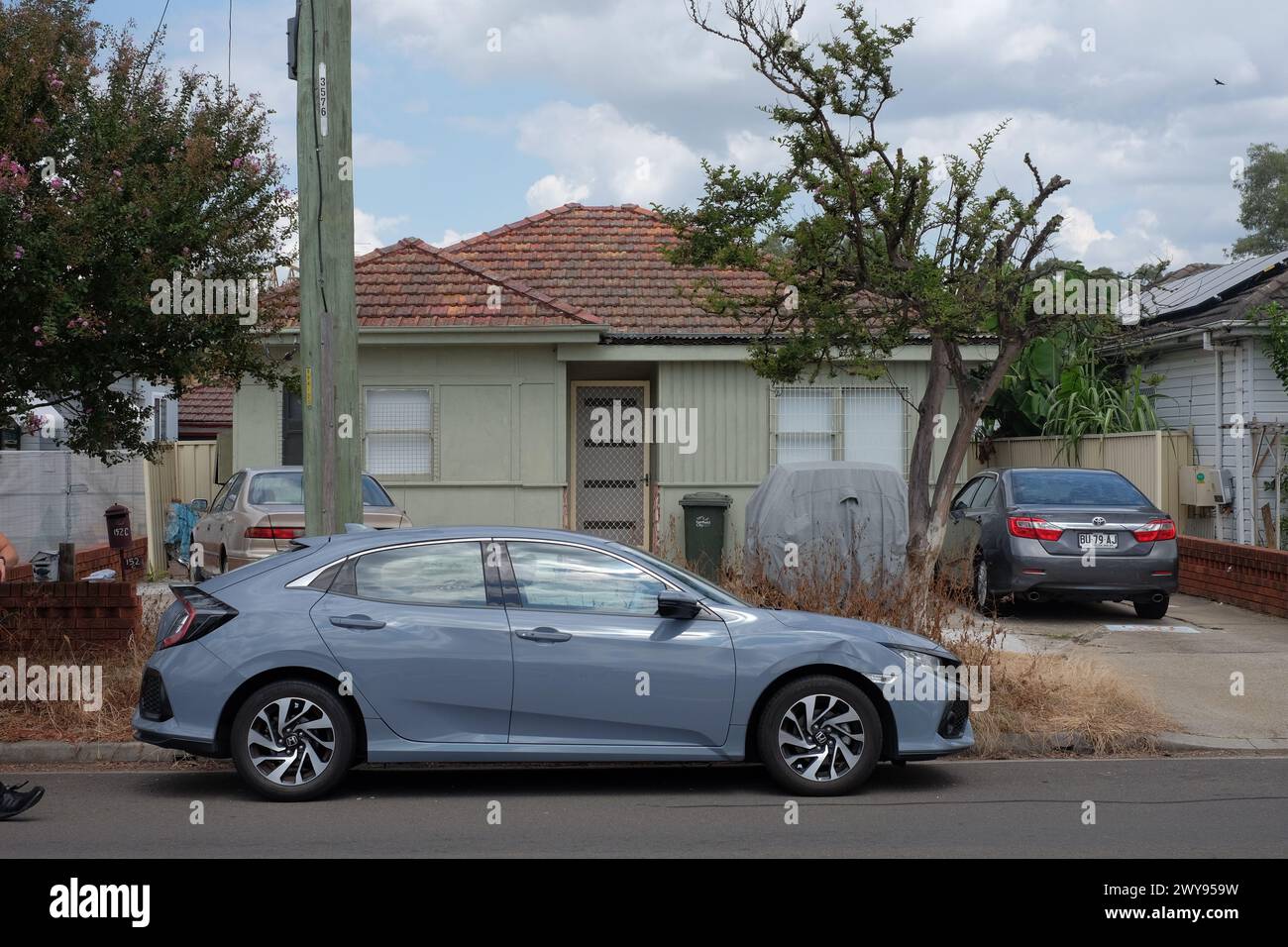 Fibro House with two cars in the driveway one in the front yard and one on the street in the Western Sydney suburb of Canley Vale Stock Photo