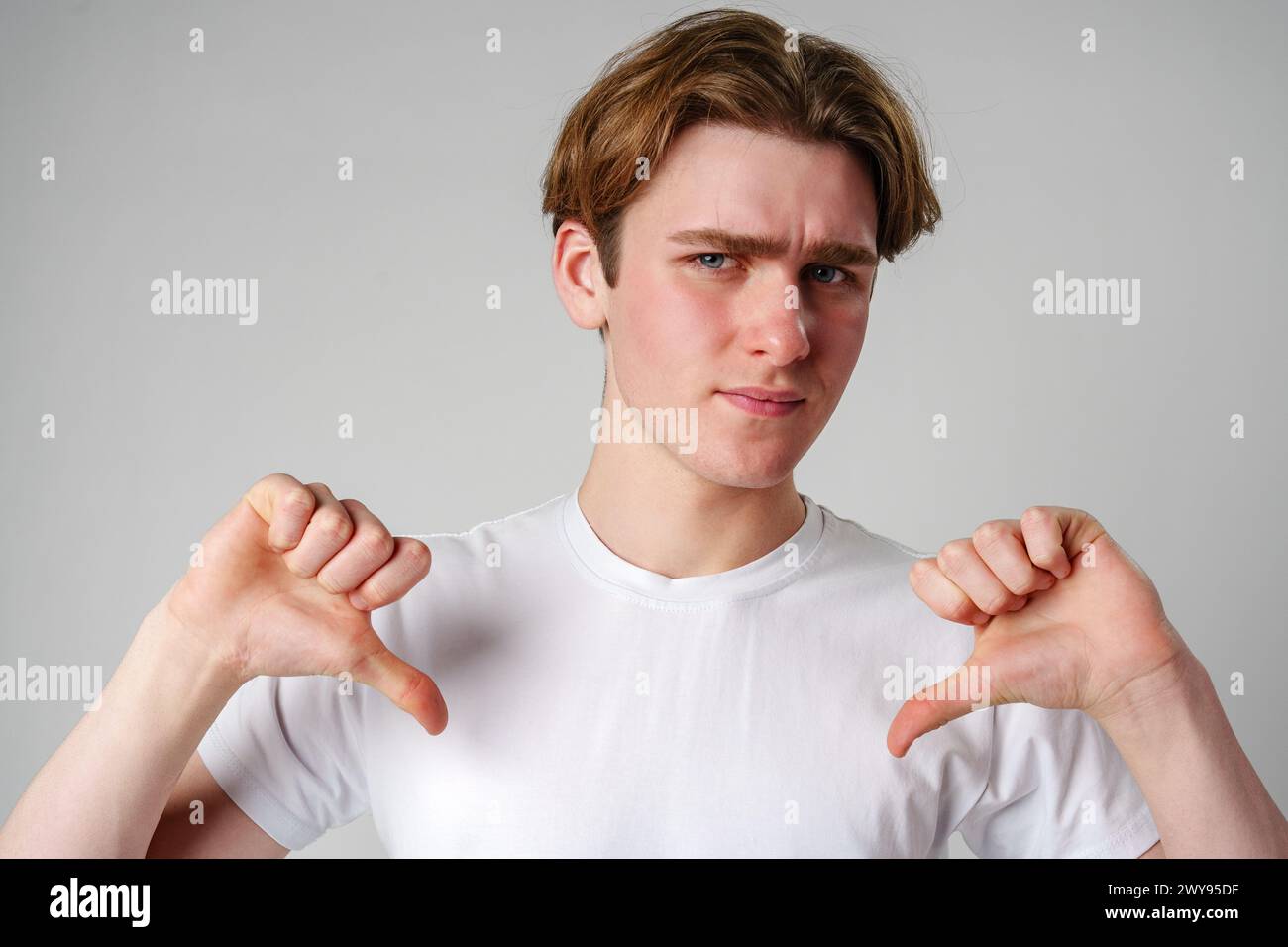 Young Man Giving Thumbs Down Gesture Against Plain Background Stock Photo