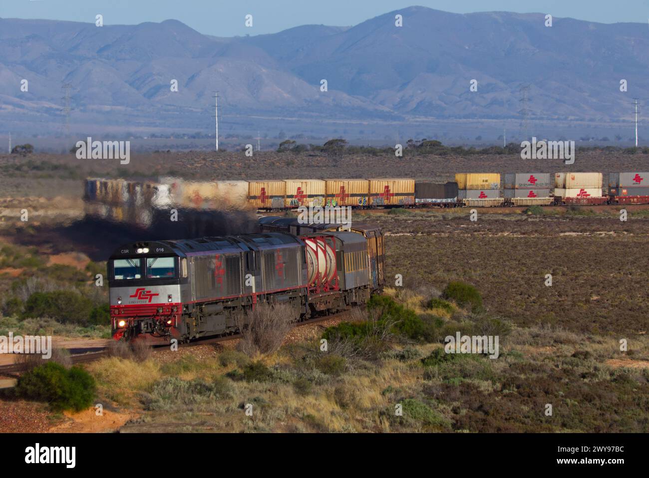 Freight train hauling cargo containers through a desert with mountains ...