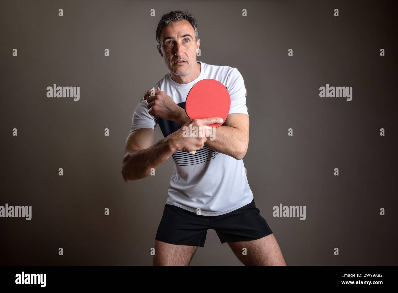 Portrait of a concentrated ping pong player waiting to receive a ball on isolated gray background. Stock Photo