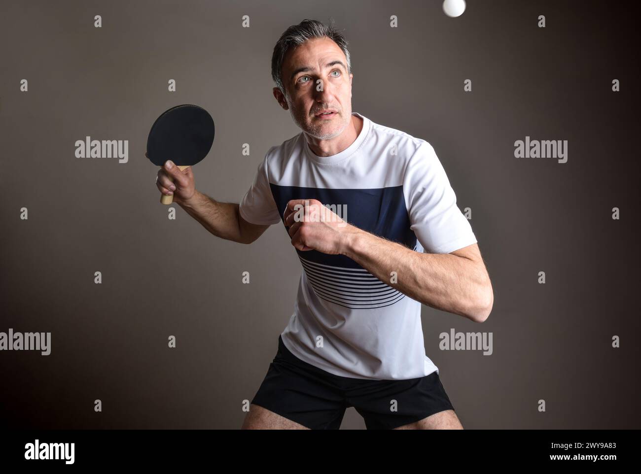 Detail of a professional ping-pong player going to hit a white ball on an isolated gray background. Stock Photo