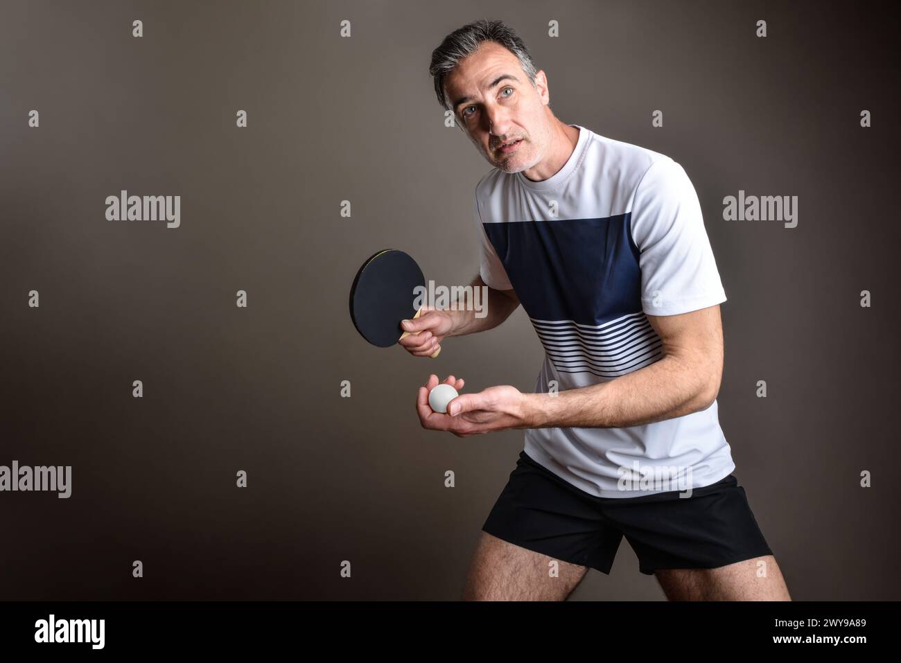Portrait of ping pong player ready to make a serve with an orange ball in his hand on gray isolated background. Stock Photo