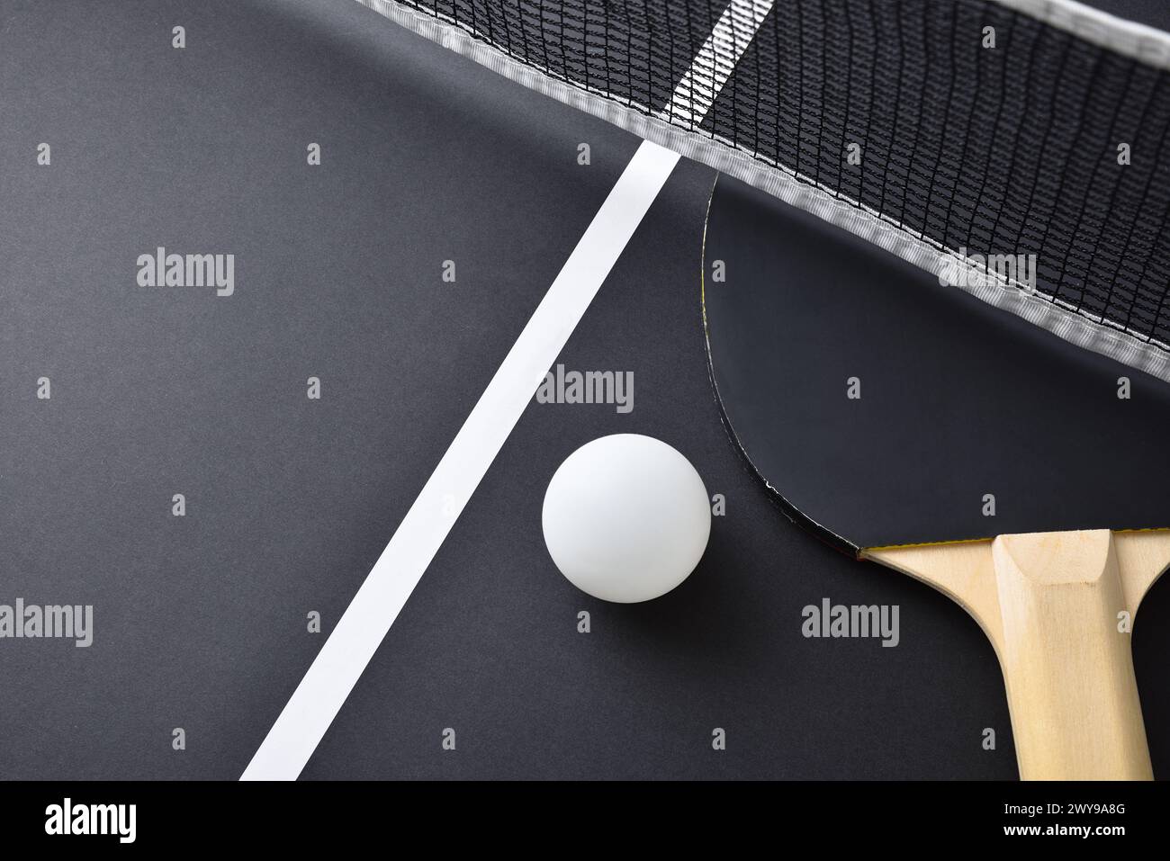 Detail of ping pong paddle with black rubber and white ball on black playing table. Top view. Stock Photo