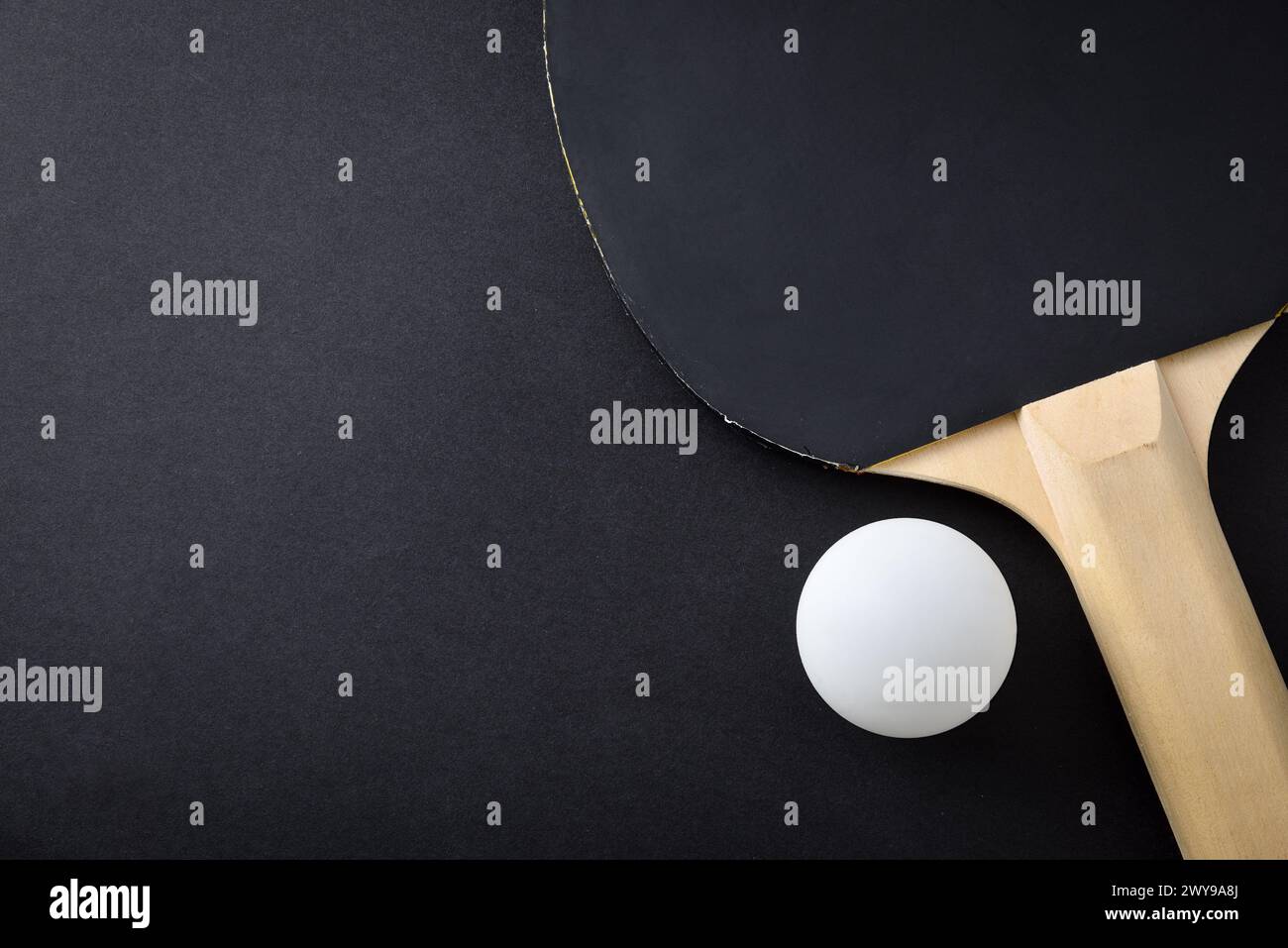 Detail of ping pong paddle with black rubber and white ball on black playing table. Top view. Stock Photo