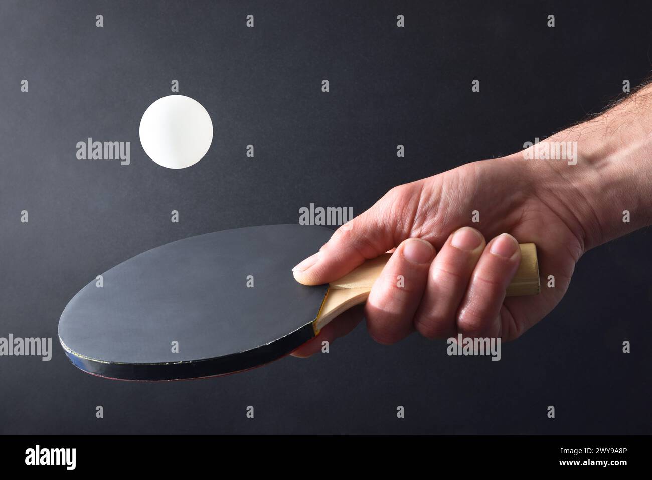 Detail of ping pong player hitting a white ball with the black rubber part of a paddle on black isolated background. Front view. Stock Photo