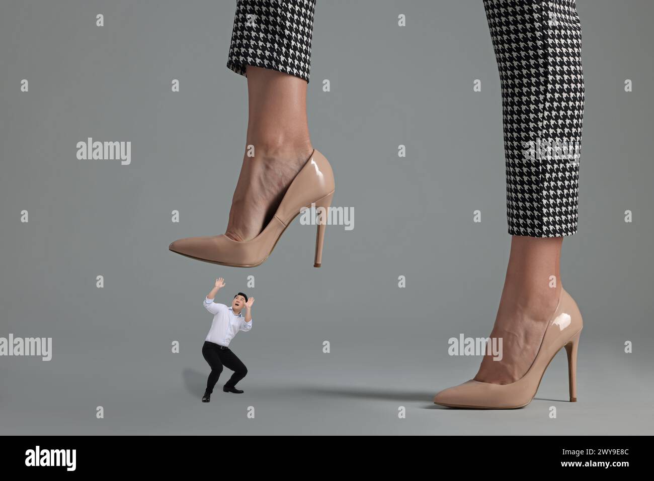 Big woman stepping onto small man on grey background Stock Photo