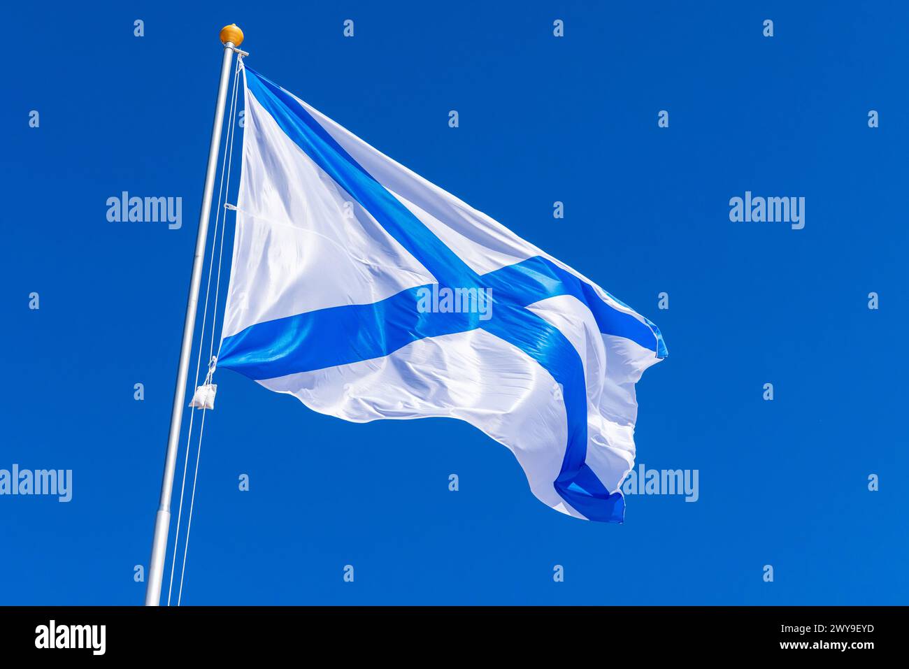 Ensign of the Russian Navy is waving on wind under blue sky, also known as the St. Andrews flag. This is the stern flag of the ships of the Russian Im Stock Photo