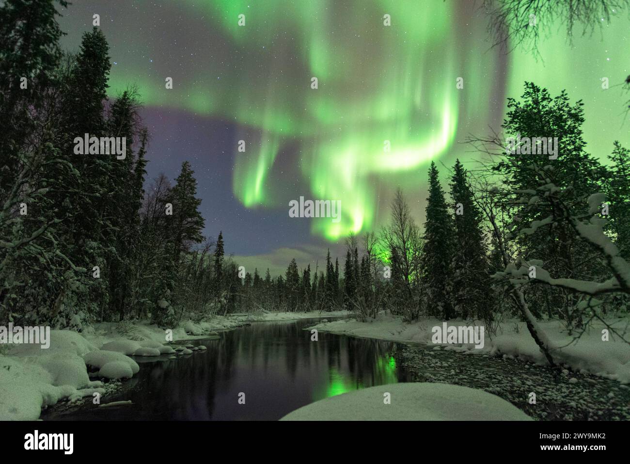 Northern Lights Aurora Borealis reflecting in the calm water of a river, starry clear sky above the forest covered with snow, Akaslompolo, Pallas-Ylla Stock Photo