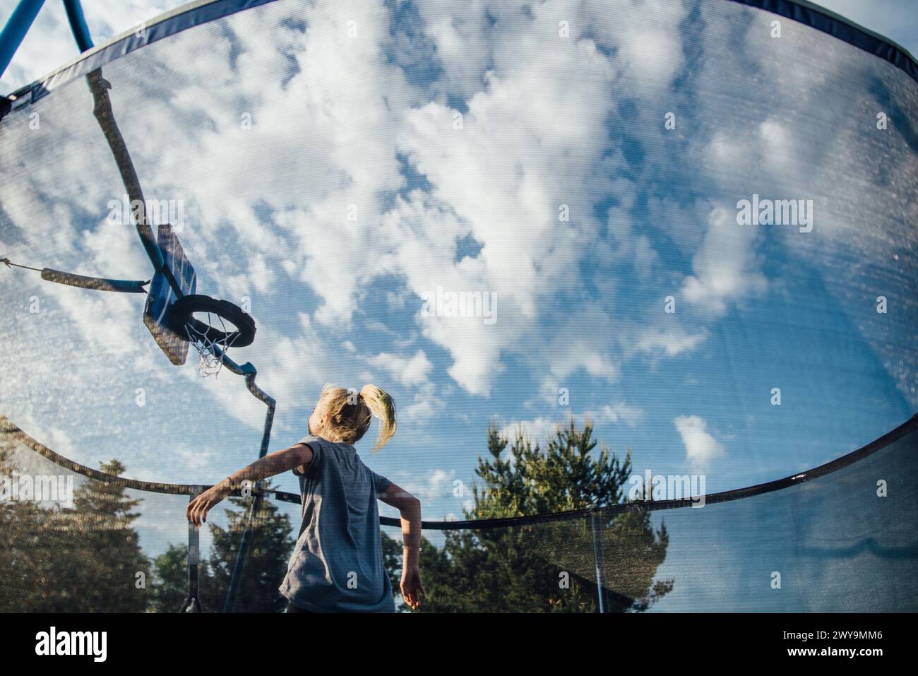 Girl playing basketball on trampoline with wide view of clouds in sky Stock Photo