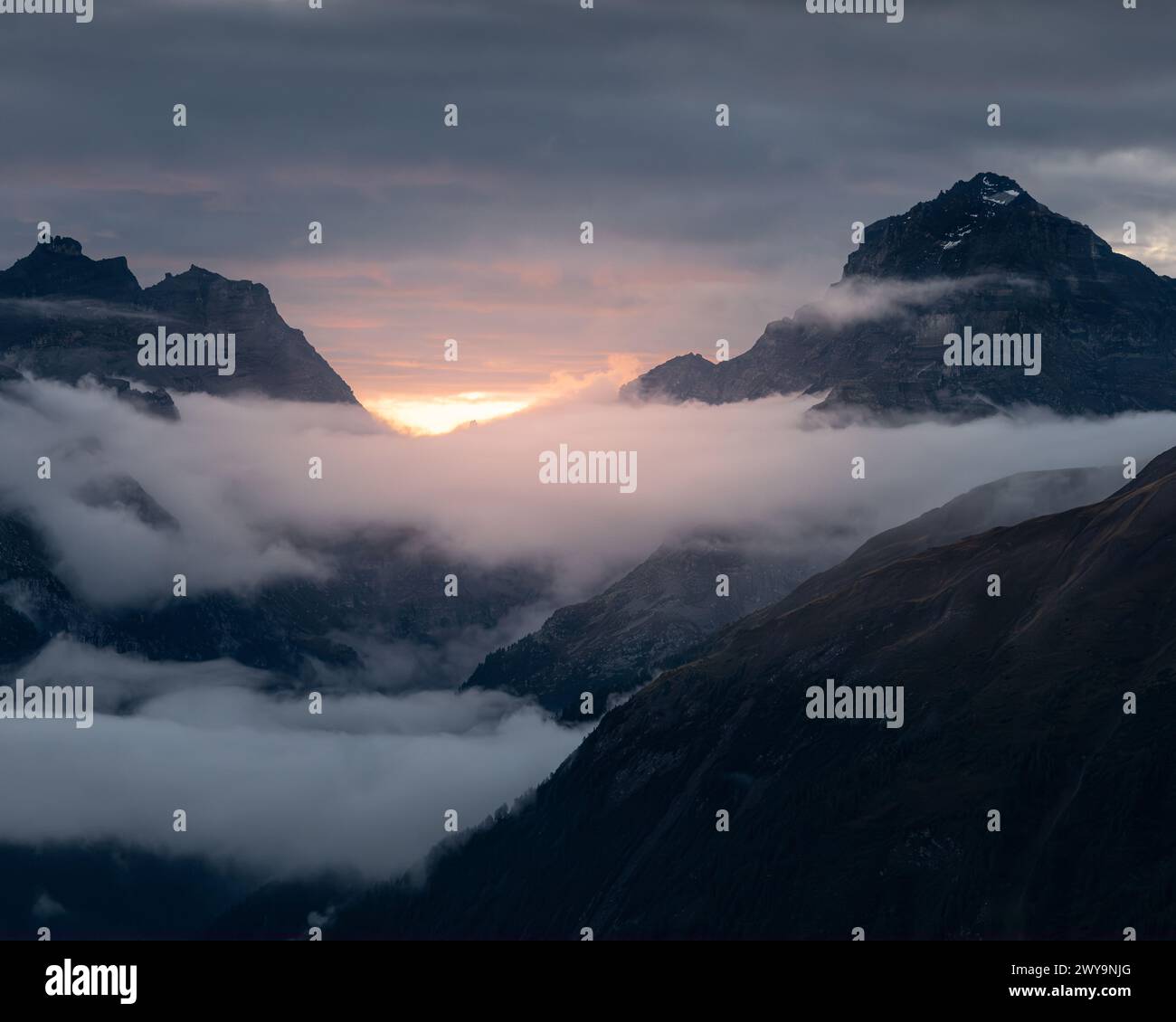 A dramatic sunset over mountains shrouded in clouds Stock Photo