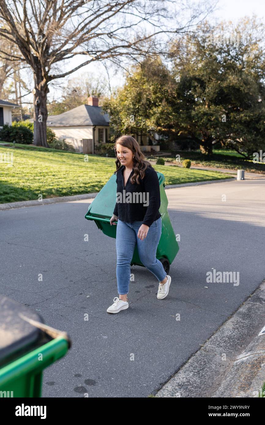 Woman rolling recycling bin on suburban street Stock Photo
