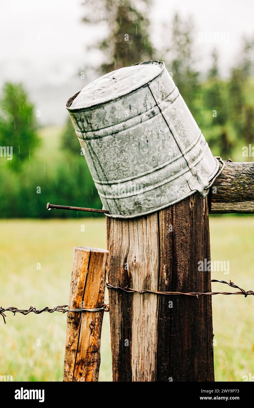 Upside down tin bucket atop wooden fence on rainy day Stock Photo