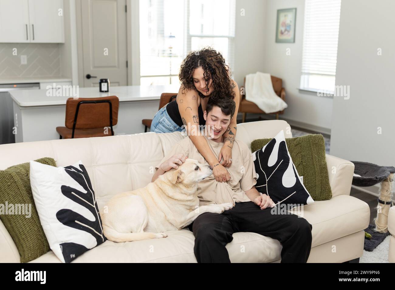 Laughing couple plays with their dog on a cozy sofa Stock Photo