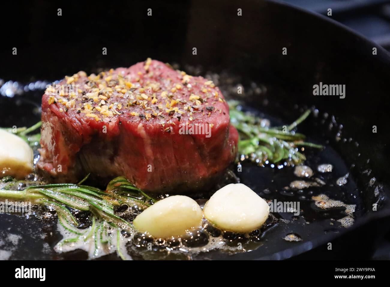 Seasoned raw filet mignon searing in cast iron skillet Stock Photo