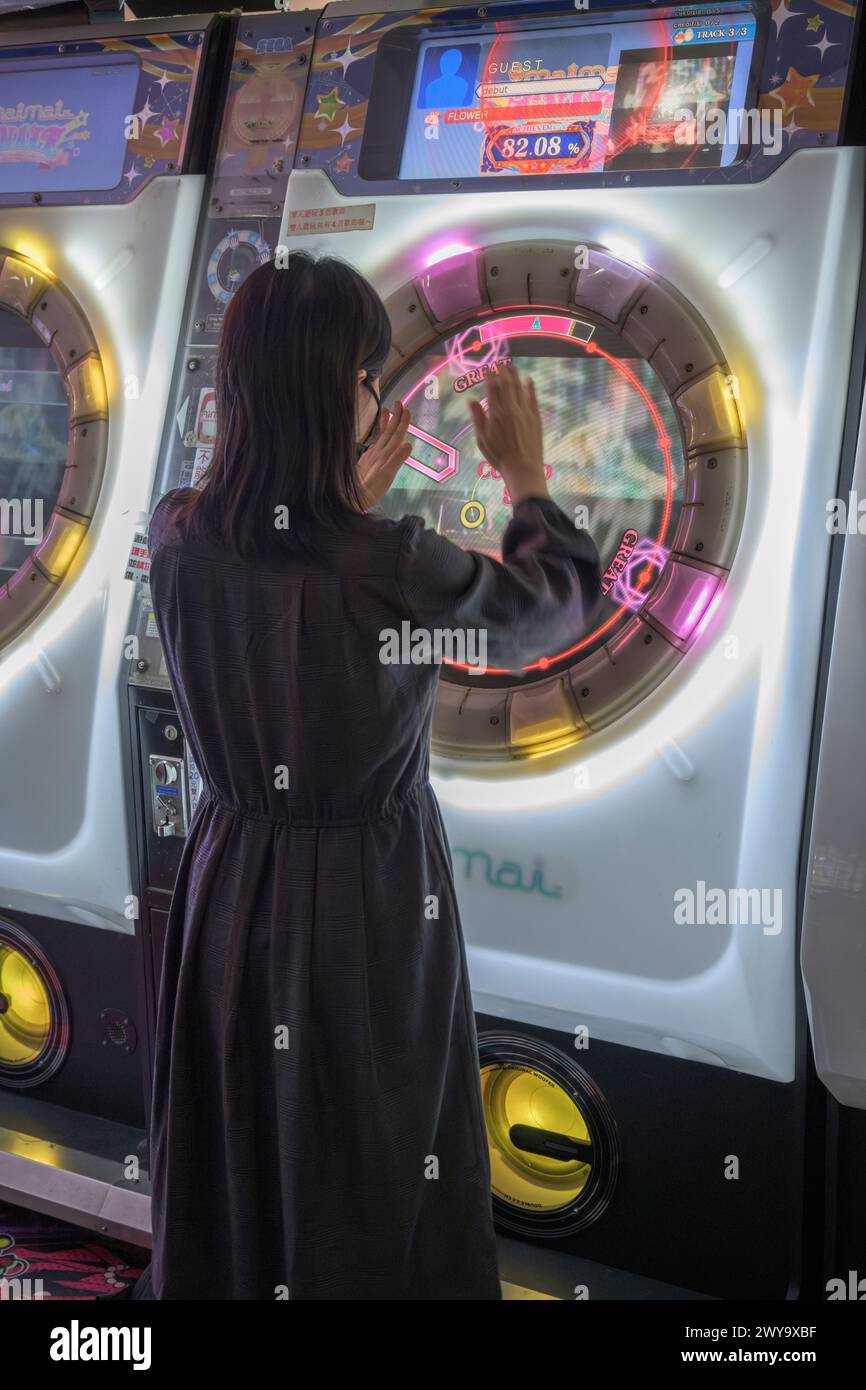 Girl engaged in intense arcade gaming on a neon-lit rhythm machine, enjoying leisure time in Taipei city mall Stock Photo