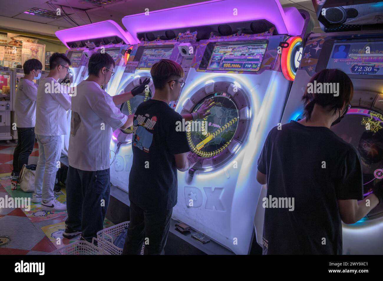 Group of friends engaged in intense arcade gaming on a neon-lit rhythm machine, enjoying leisure time in Taipei city mall Stock Photo