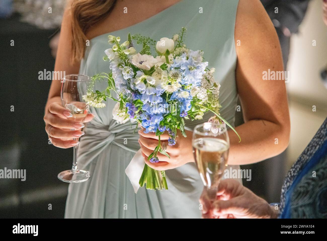 A bridesmaid holding a bouquet of flowers and a glass of champagne at a wedding at Dulwich Picture Gallery in London, UK Stock Photo