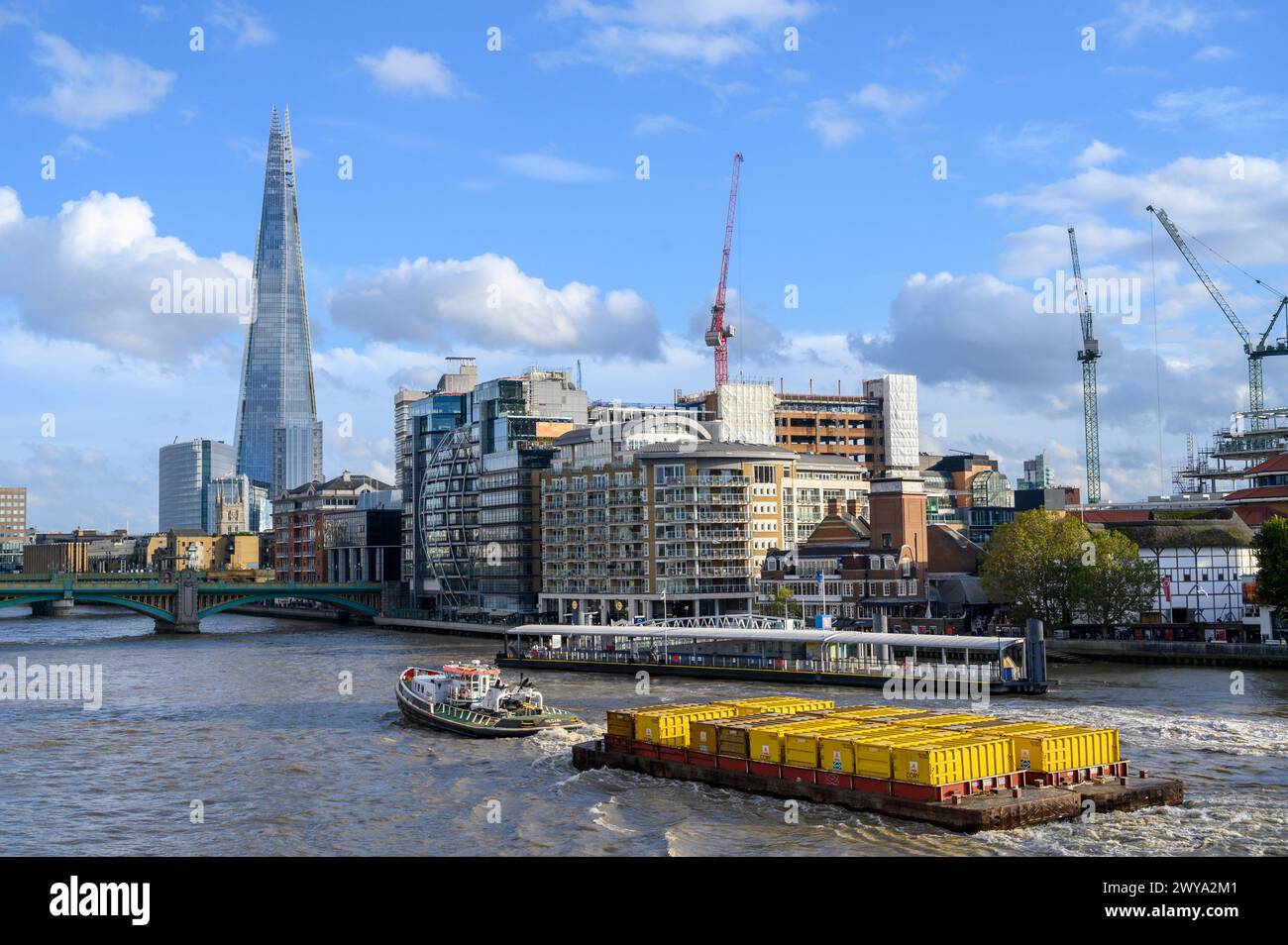 Tugboat towing yellow containers full of compacted rubbish towards  Southwark Bridge on the River Thames in London, England. Stock Photo
