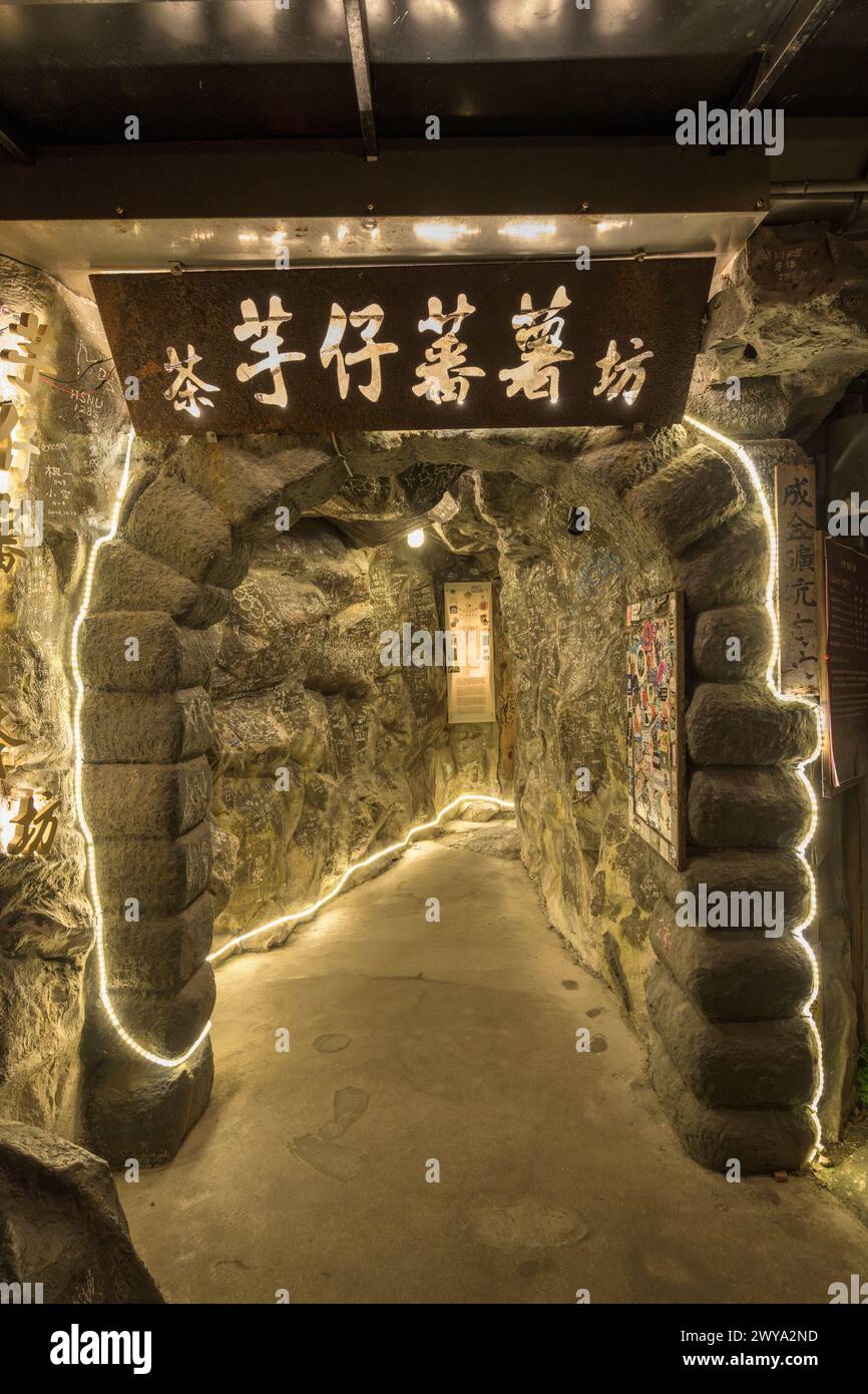 The warm glow of lights invites you into a mysterious rock tunnel with Chinese characters at the entrance Stock Photo