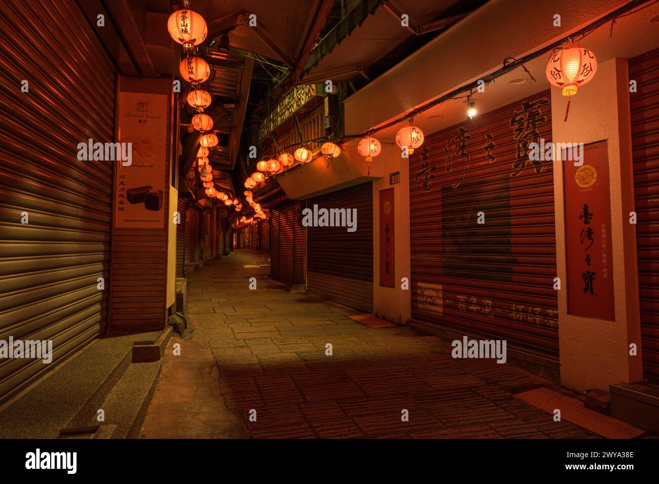 A narrow, quiet alley decorated with lanterns leading to a traditional market with its closed shops on the streets of Jiufen Stock Photo