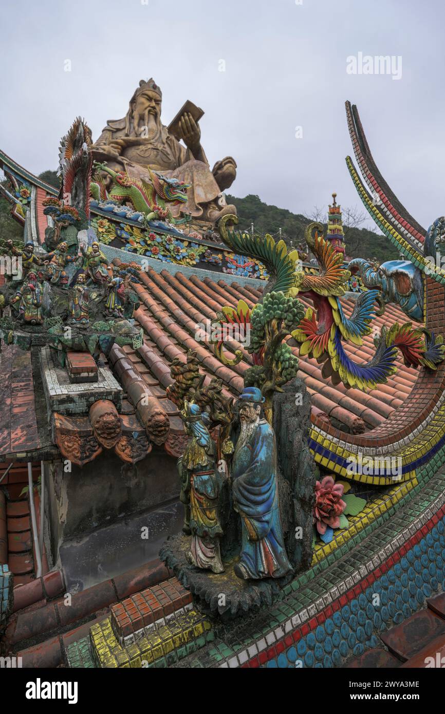 View showcasing a dragon-decorated Chuen Ji Hall temple roof and a colossal statue in the background Stock Photo