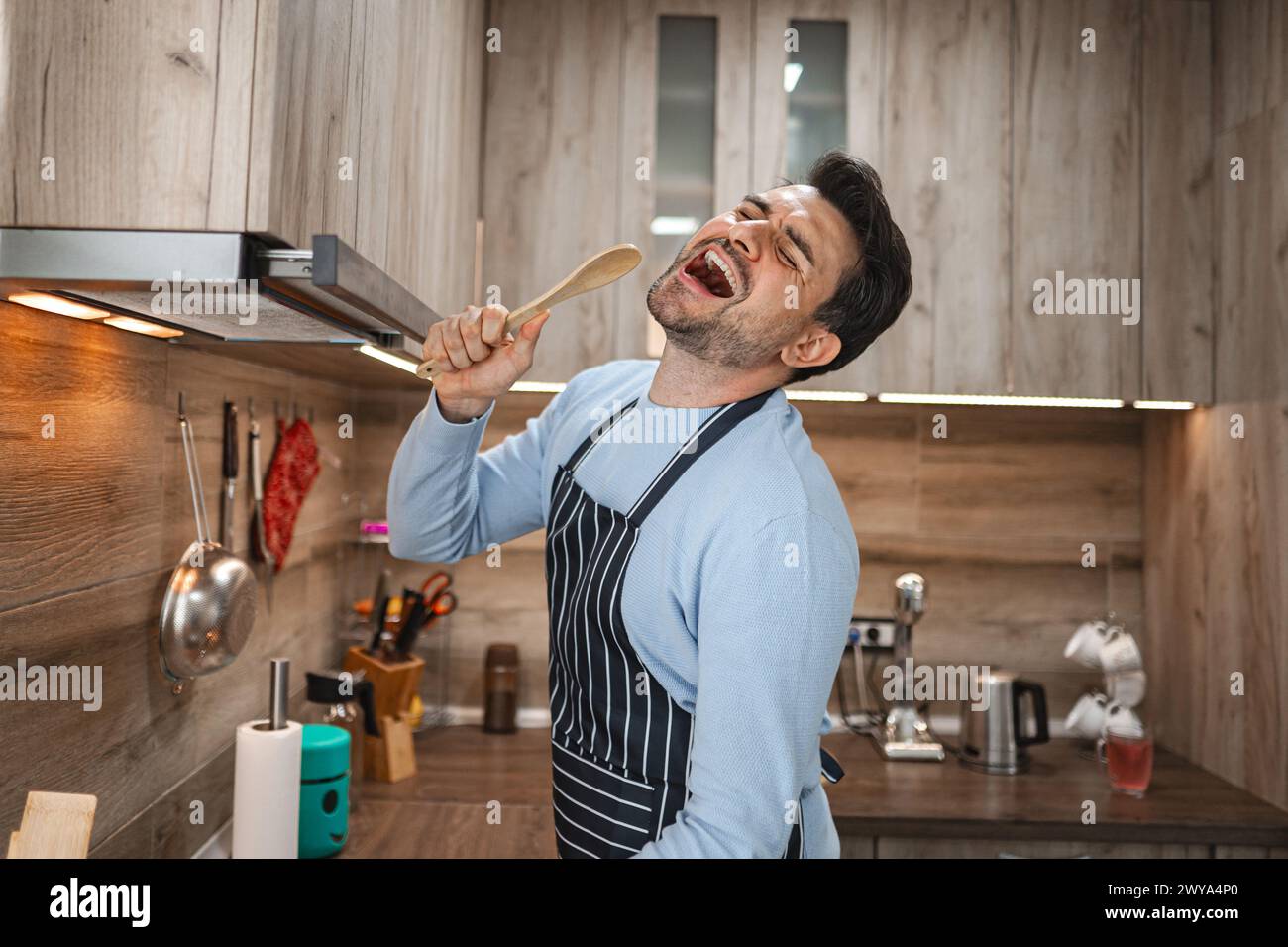 Man holds a spatula in his apron and sings in the kitchen Stock Photo
