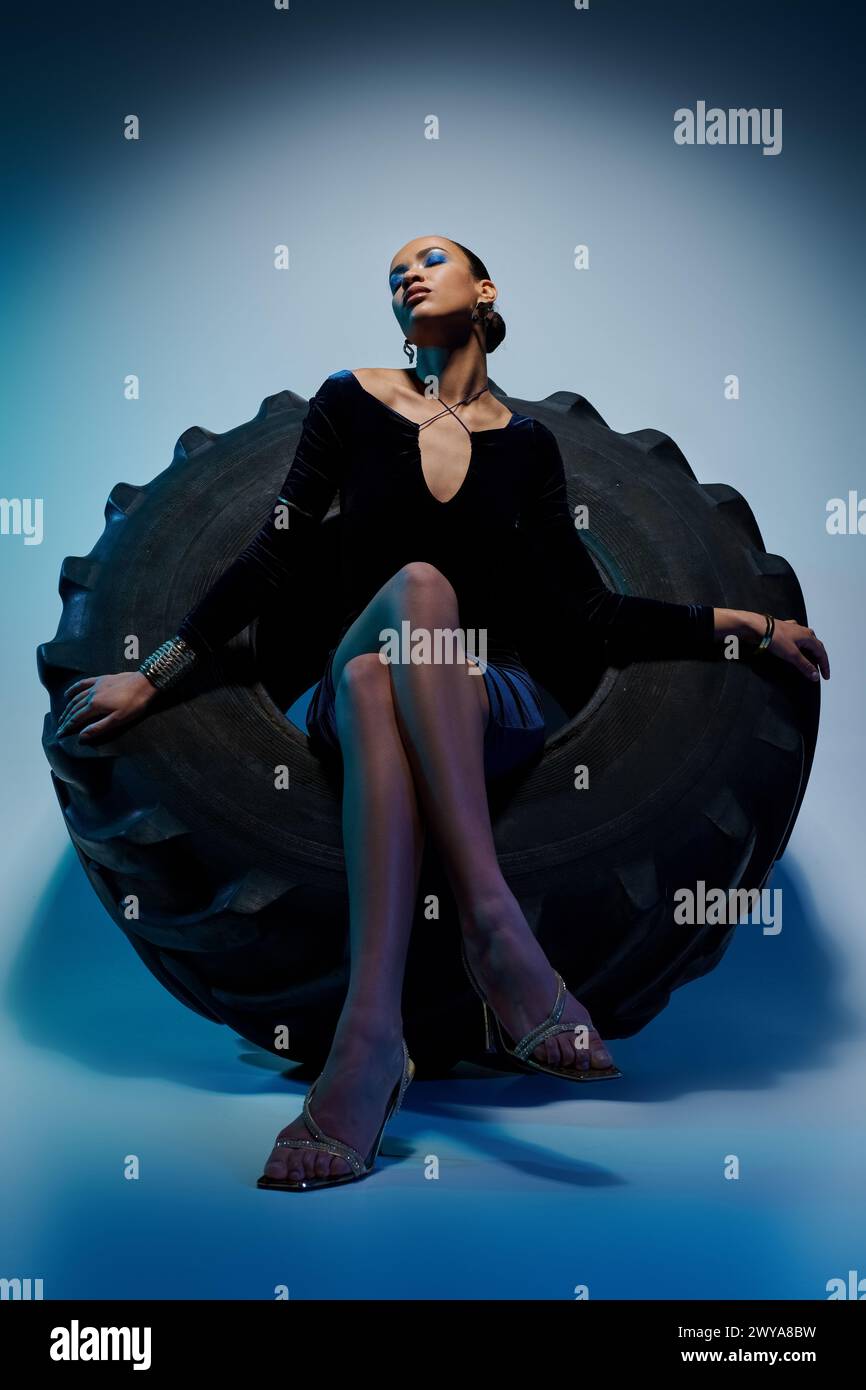 Young African American woman in a black dress gracefully sitting on a black object. Stock Photo