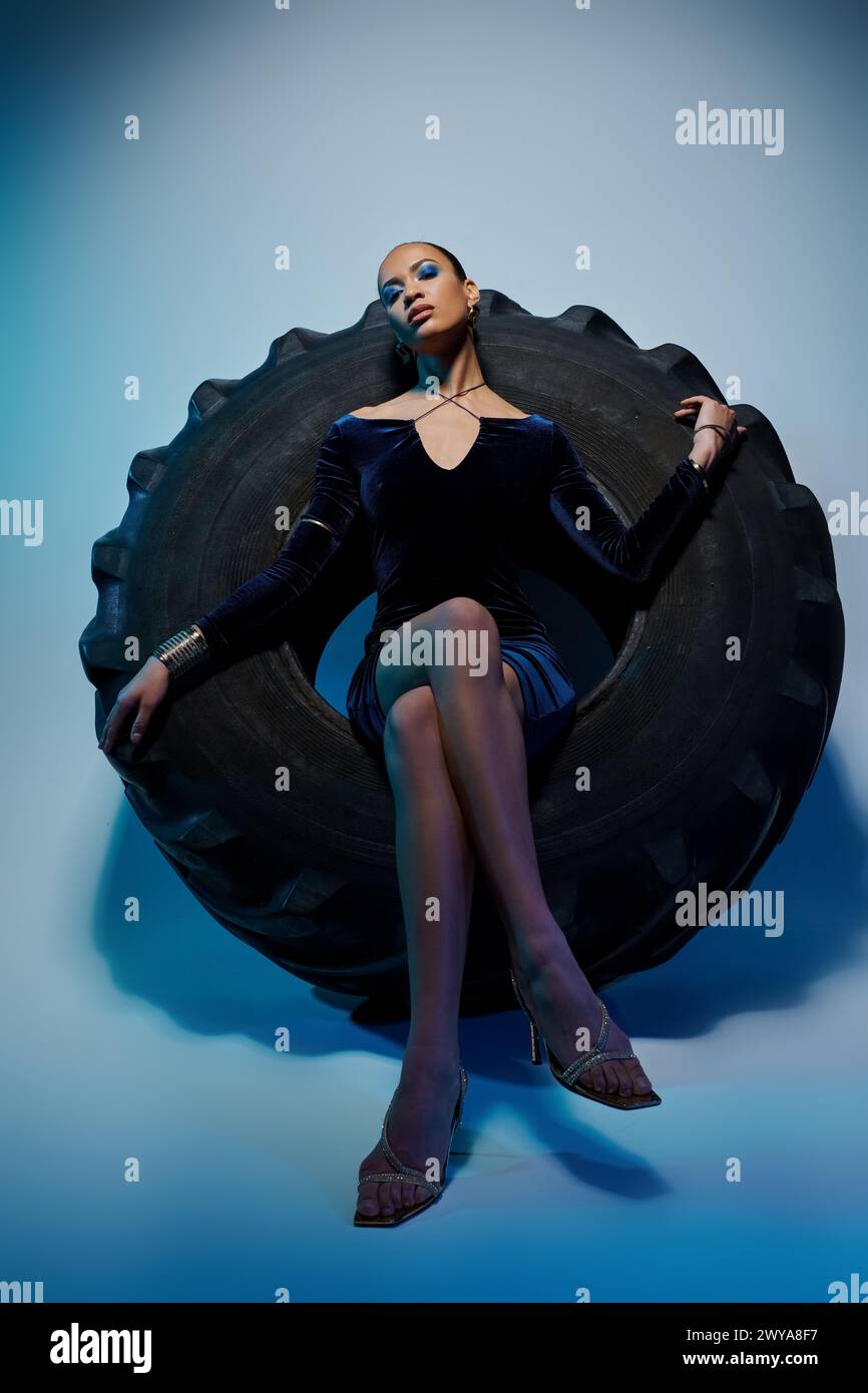 A young African American model in a black dress sitting on a giant tire. Stock Photo