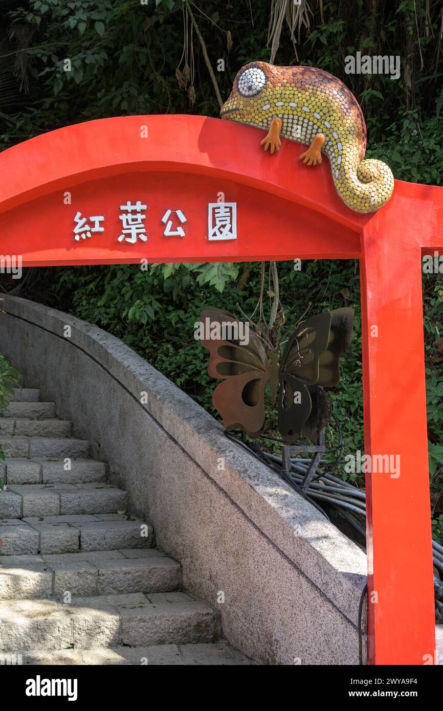 A mosaic chameleon sculpture perched atop a bright red traditional arch with Chinese characters in Guanziling Hot Spring Stock Photo