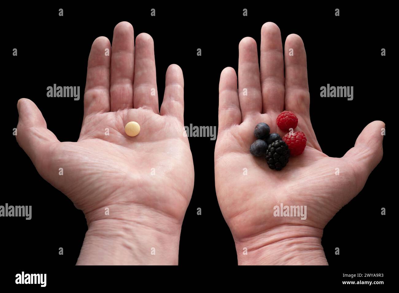 Two hands presenting berries in the right one, and a pill in the left one, representing choices in nutrition and dietary concept. Black background. Stock Photo