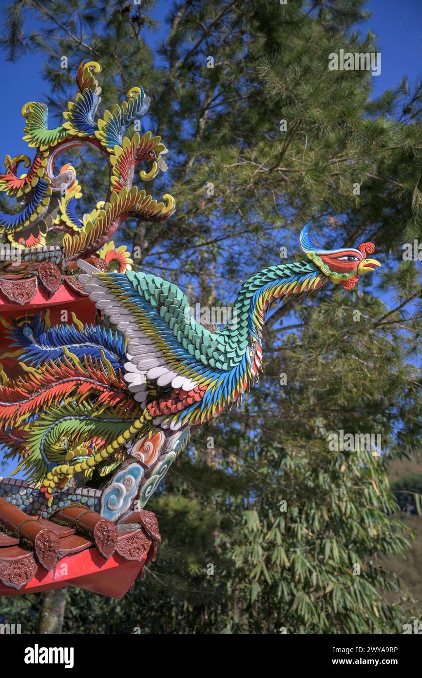 A vibrant dragon sculpture adorning a temple roof with a blue sky and pine tree backdrop Stock Photo