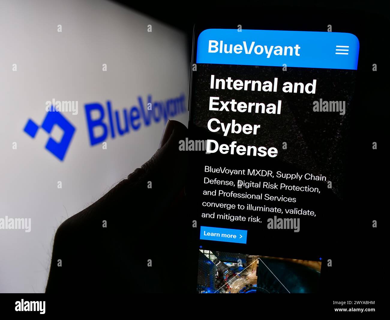 Person holding cellphone with website of US cyber defense platform company BlueVoyant LLC in front of logo. Focus on center of phone display. Stock Photo