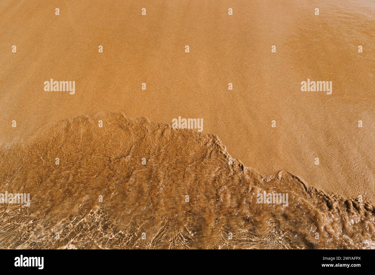 sandy beach with waves rolling in, creating a beautiful natural background. beige sand contrasts with ocean waves. concept for perfumes, smells, heat Stock Photo