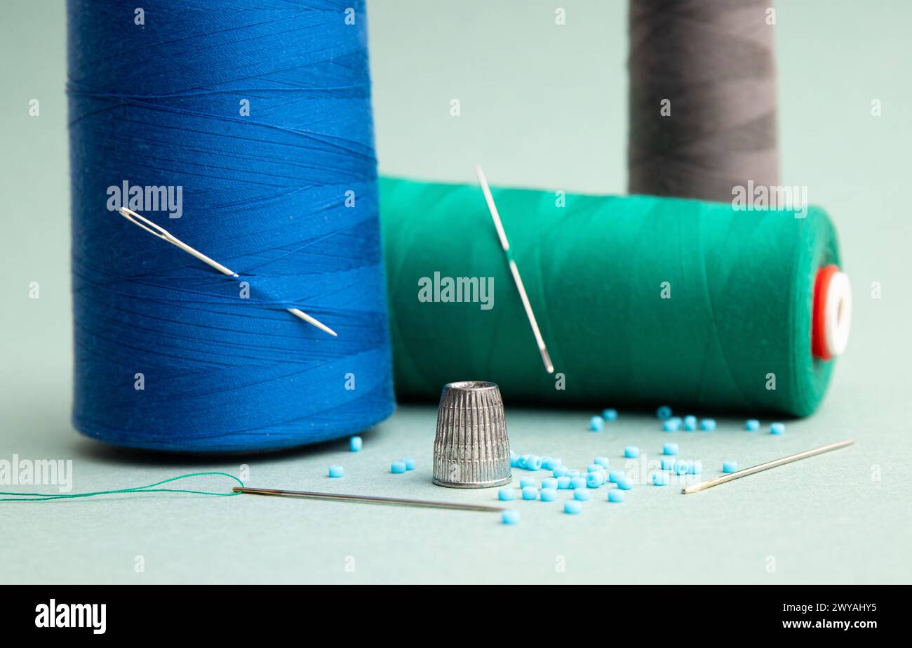 Still life of sewing items, metal sewing thimble finger protector or finger shield thimble, thread rolls, needle and beading at home. Arts and crafts. Stock Photo