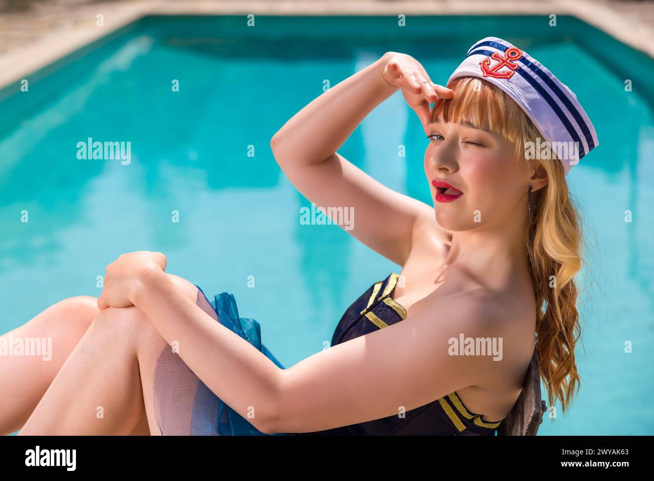 Attractive young woman dressed in a sexy sailor costume as a pinup girl on the edge of a swimming pool Stock Photo