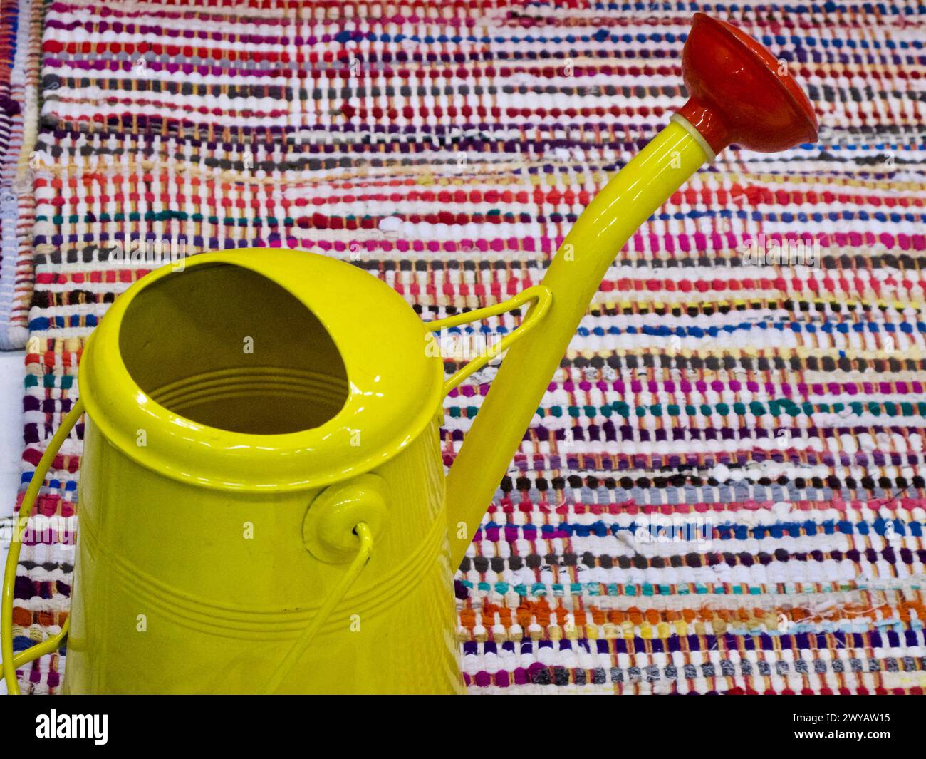 Metal outdoor watering can on a striped colourful carpet on the balcony in spring. Stock Photo
