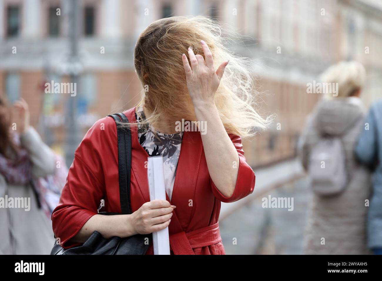 Blonde woman fix her long hair on a street, wind in city Stock Photo