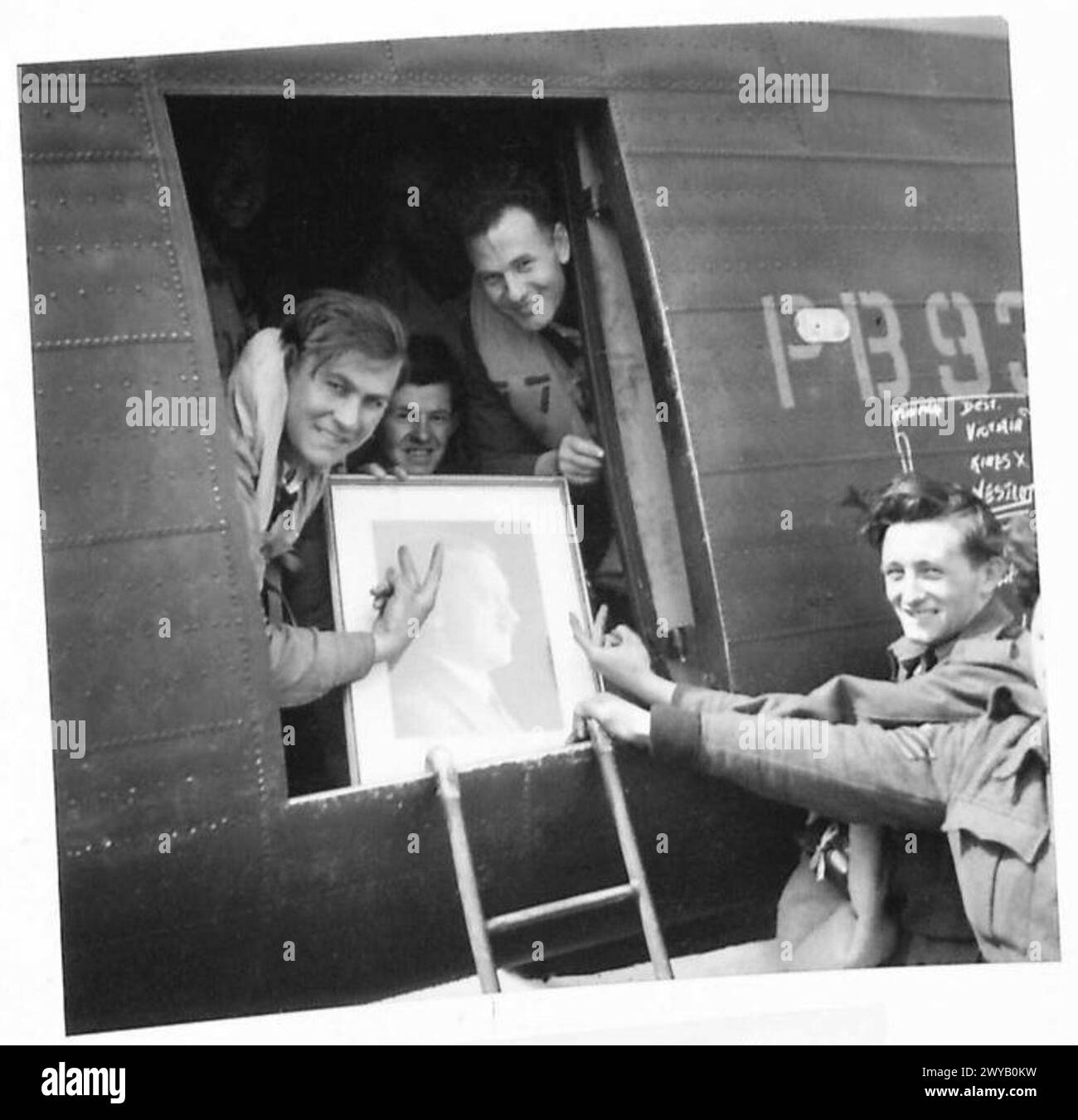 EX-BRITISH POWs RETURNING HOME BY AIR - Original wartime caption: Smiling happy faces, show the 'V' sign to a portrait of Hitler. Photographic negative , British Army, 21st Army Group Stock Photo