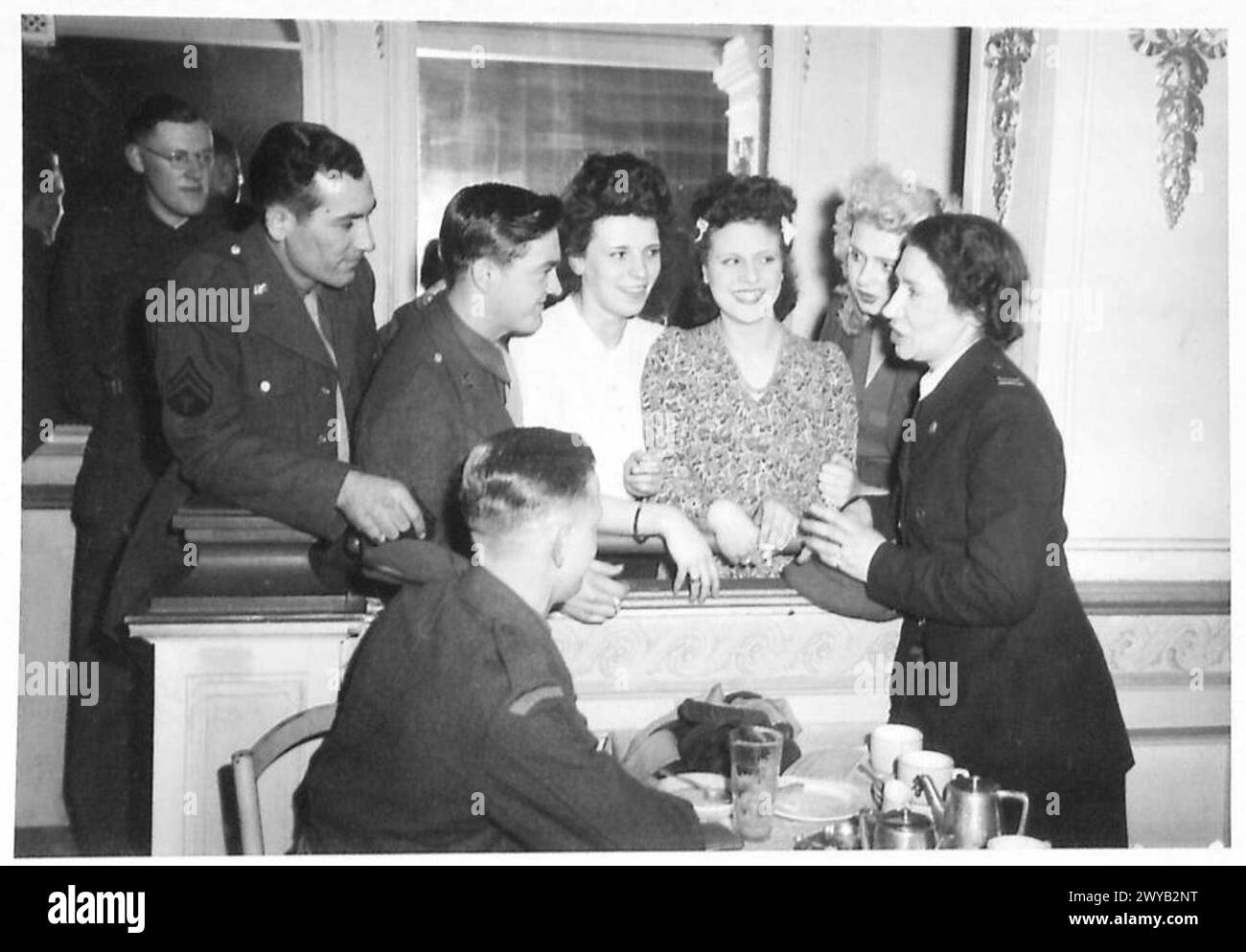 THE '21' DANCE CLUB, BRUSSELS - Original wartime caption: Mrs Robinson, one of the Welfare workers, smooths out a language difficulty between three Belgian girls and two Americans. Americans are Cpl C. Cook of Mississipi and Cpl. S. Gomore of New York. Mrs Robinson had an exciting story to tell them she is married to an Englishman (in Surrey) and when the Germans marched into Belgium in 1940, she stayed behind to do Red Cross work. For helping British men to escape she was given hard labour for eight years by the Germans, of which she served 20 months. The Germans executed the men with whom sh Stock Photo